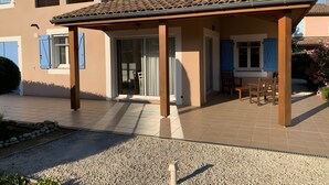 A covered patio area with a tiled roof, a door leading to an interior space, and a seating area with chairs. - Ardèche Villa for Rent (Vallon-Pont-d'Arc)