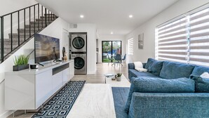A modern living space with a staircase, a kitchen, a dining area, and a large window with blinds. - Fox Palace Pool House (Fort Lauderdale)