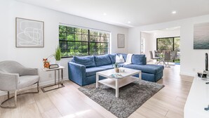 A modern living room with a blue sofa, a white coffee table, and a grey armchair. - Fox Palace Pool House (Fort Lauderdale)