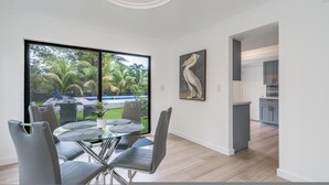 A modern kitchen with grey cabinets and a dining area with a glass table and grey chairs. - Fox Palace Pool House (Fort Lauderdale)