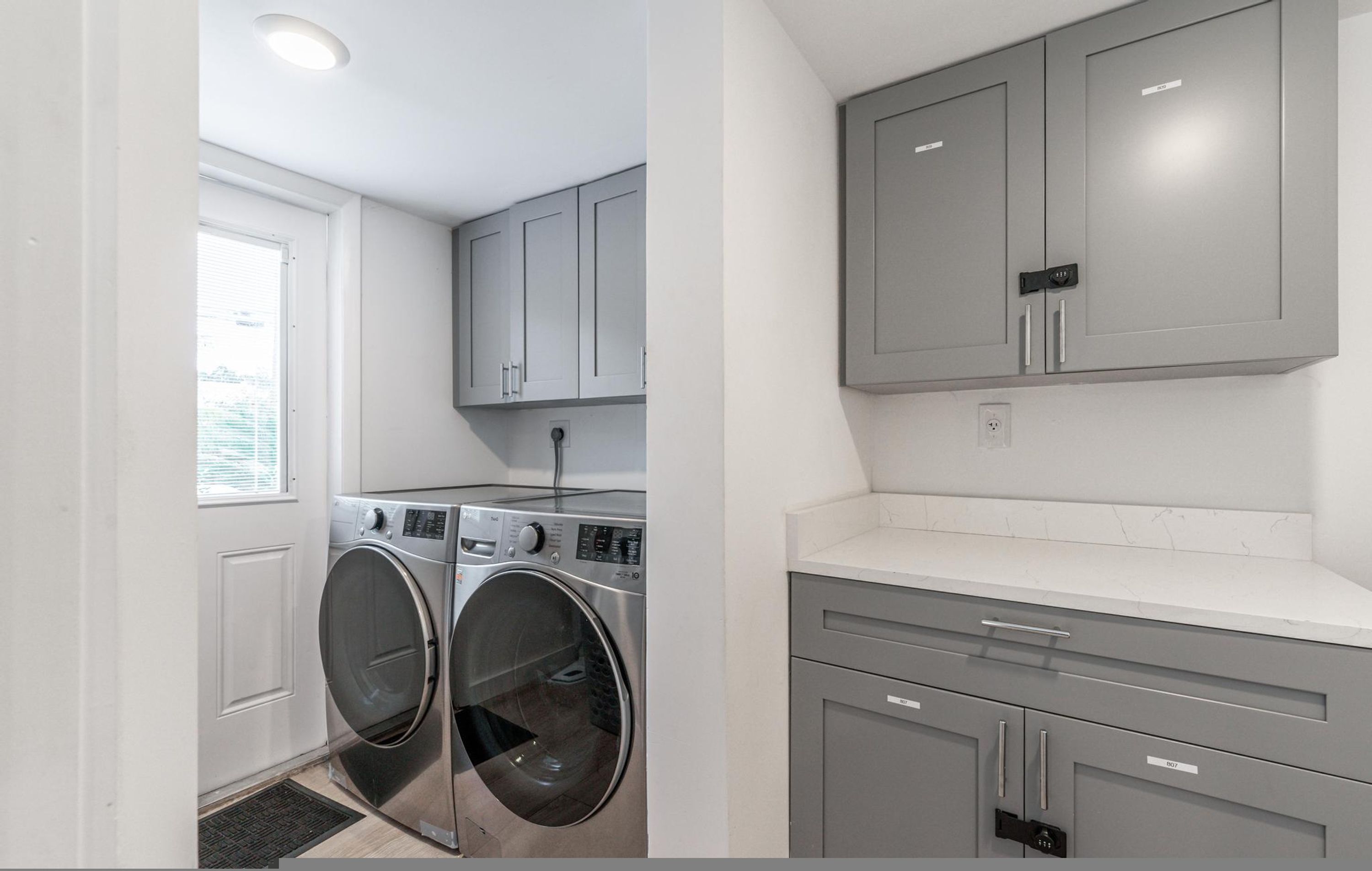 A laundry room with two washing machines, a dryer, and grey cabinets.