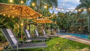 A poolside area with lounge chairs and umbrellas, surrounded by lush greenery. - Fox Of Oz- Pool Spa Oasis Villa (Fort Lauderdale)