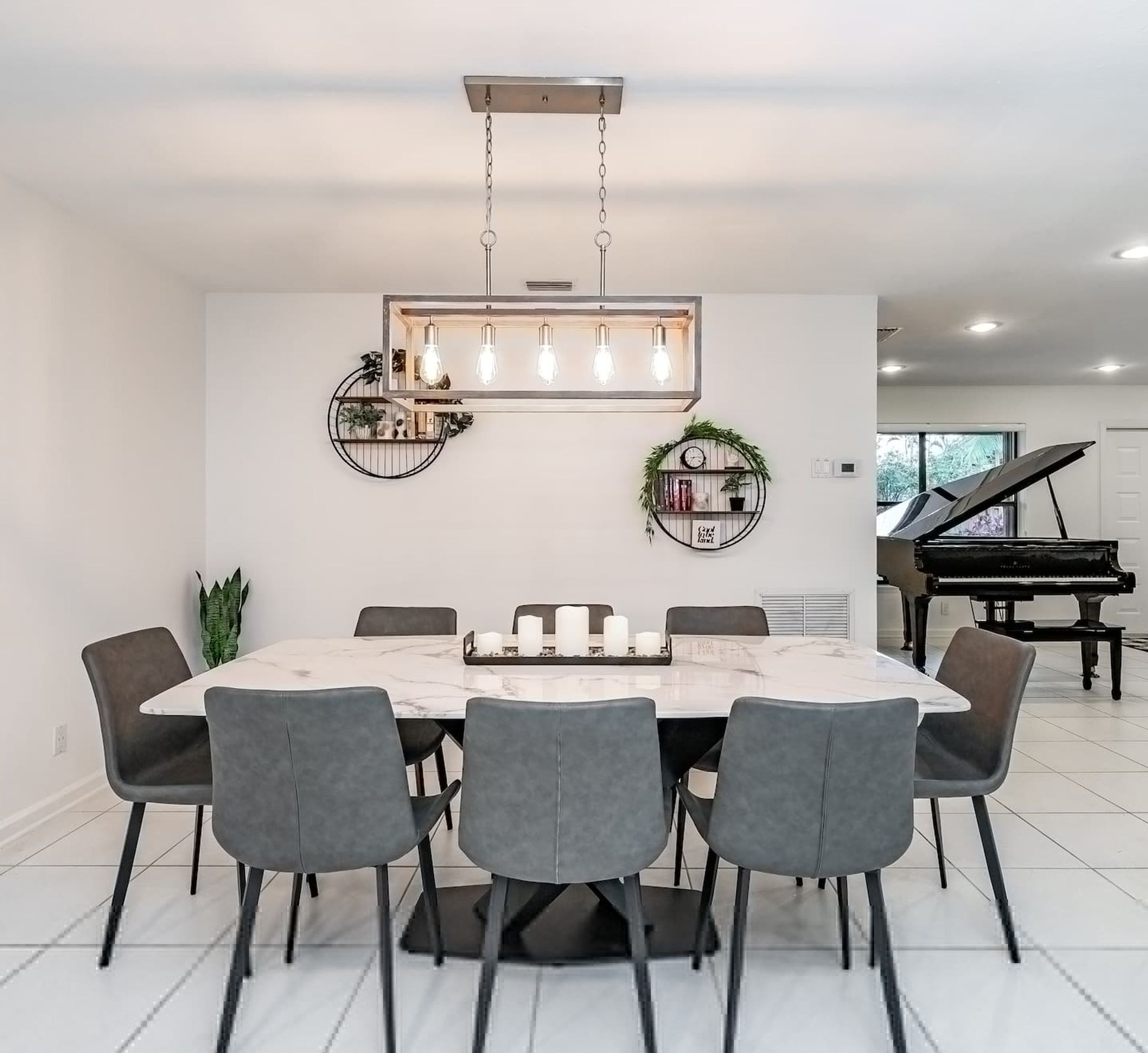 A dining room with a marble table, grey chairs, a hanging light fixture, and a piano in the background.
