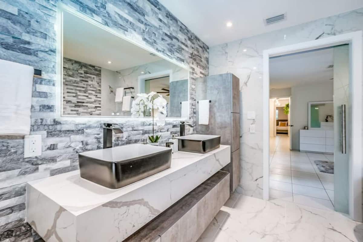 Un baño moderno con un espejo grande, dos lavamanos y una encimera de mármol.