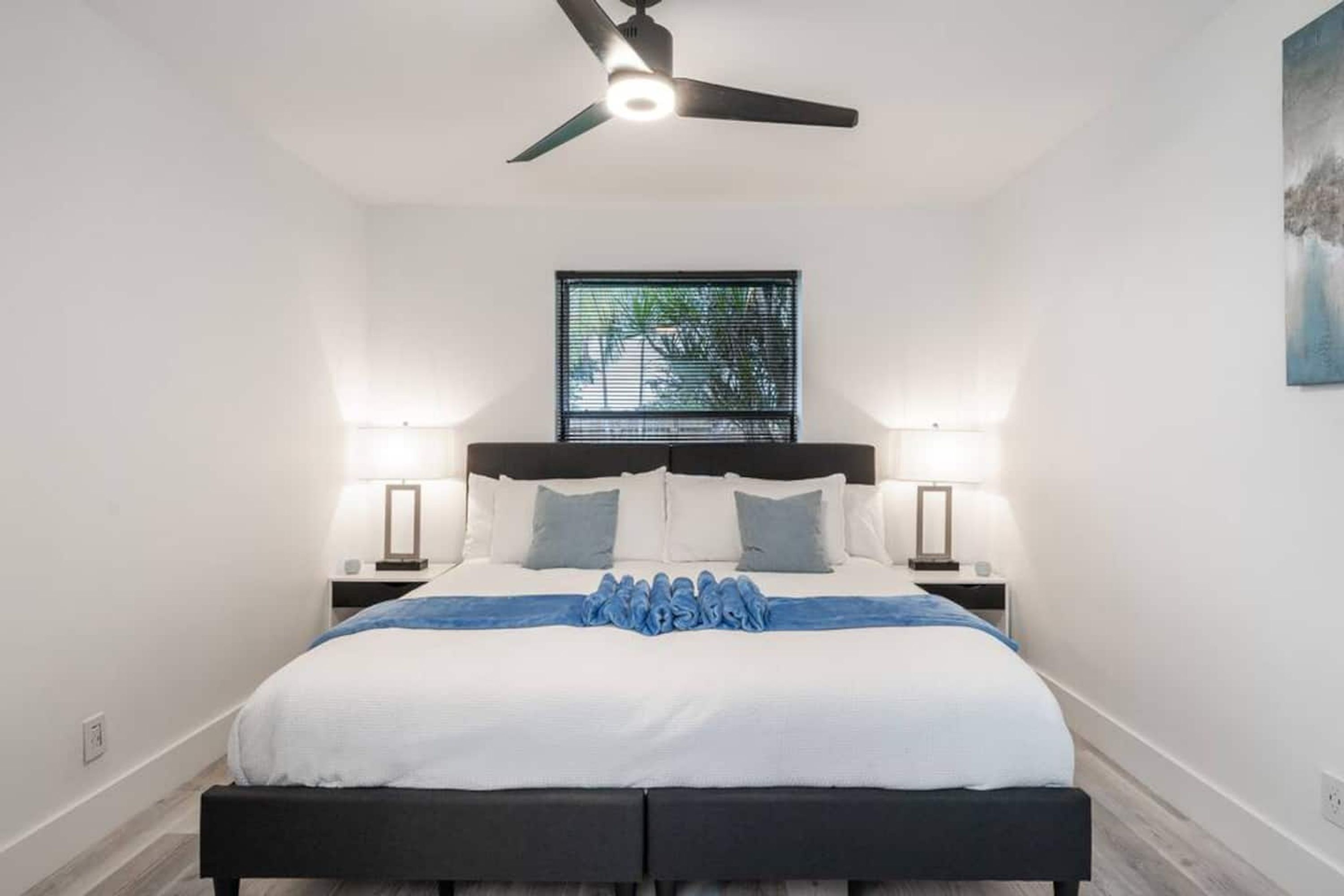 A bedroom with a bed, bedside lamps, a ceiling fan, and a window with blinds.
