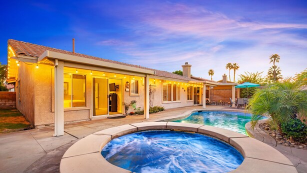 A residential property with a swimming pool, outdoor seating, and a well-lit entrance. - Private Pool & Spa | Walk to Tennis Garden (La Quinta)