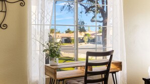 A room with a wooden desk, a chair, a potted plant, and a window with a view of a street and trees. - Private Pool & Spa | Walk to Tennis Garden (La Quinta)