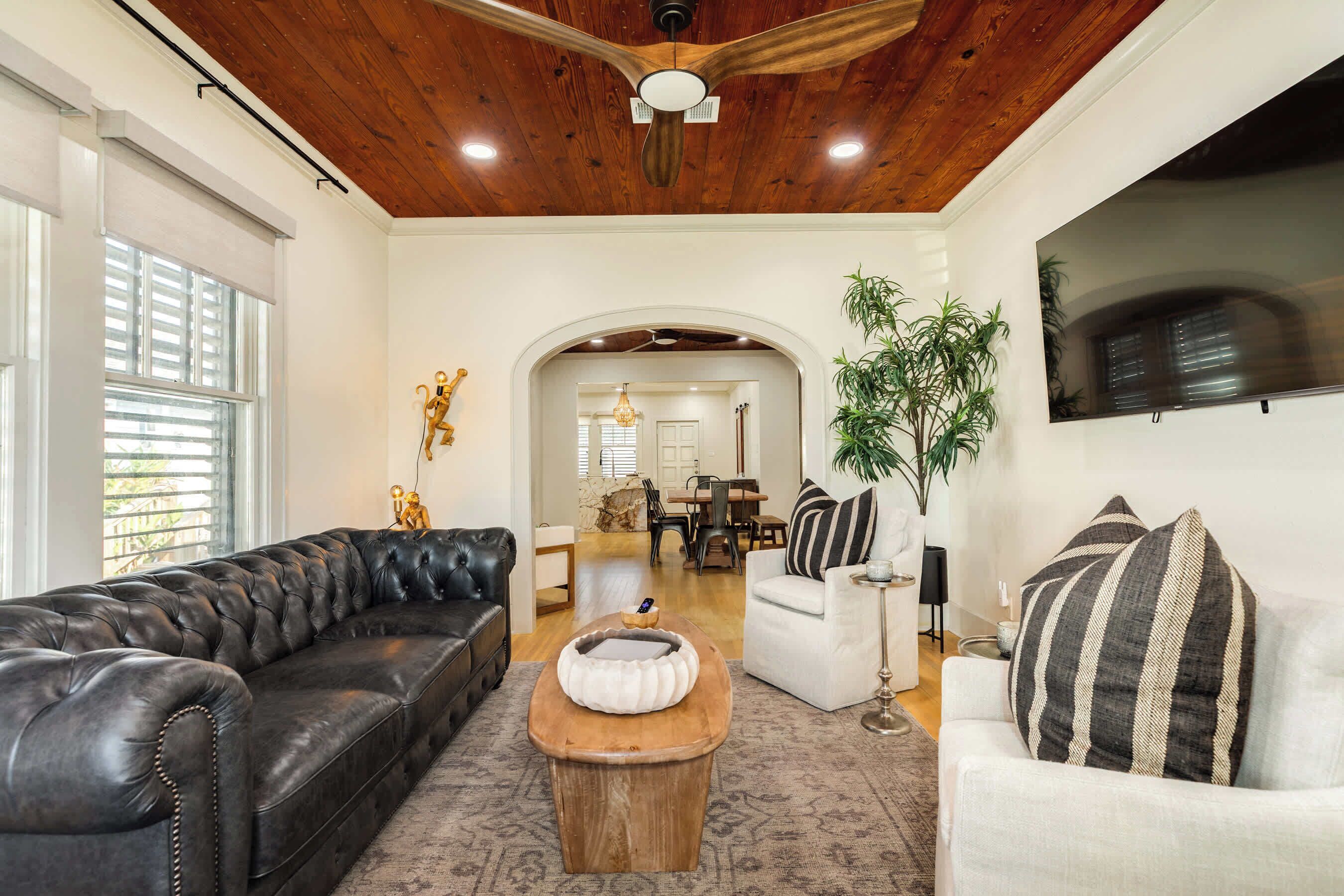 A living room with a black leather sofa, a white armchair, a wooden coffee table, and a ceiling fan.
