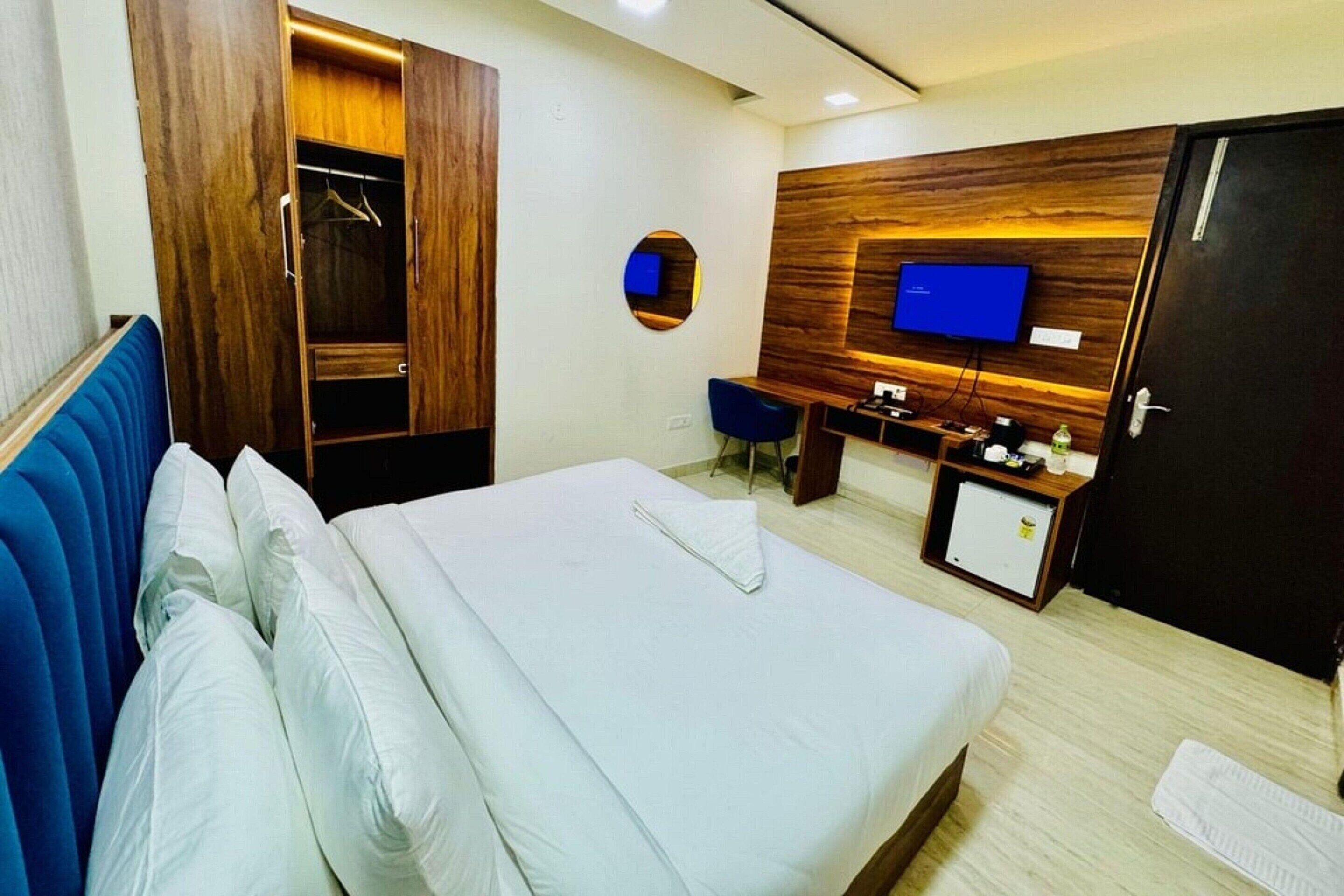 Habitación de hotel con cama, armario, escritorio con silla, televisor y un mueble pequeño.