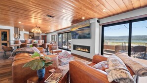 Un salón amplio con sofás de cuero, chimenea y ventanas grandes que ofrecen vistas al exterior.