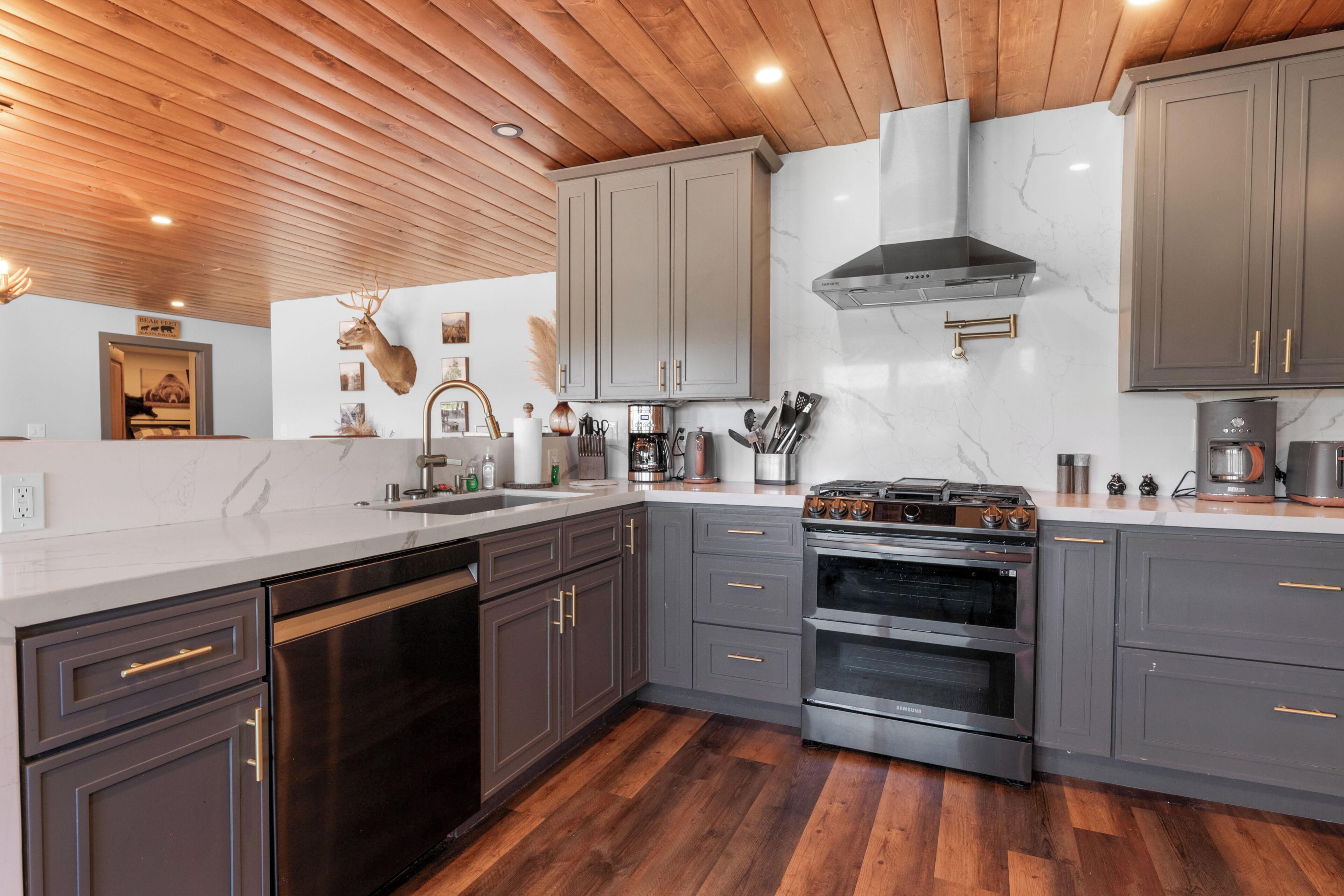 Une cuisine moderne avec des meubles gris, des appareils en acier inoxydable et un plancher en bois.