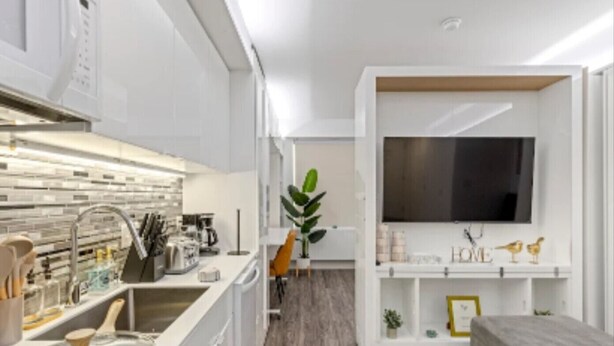 Et moderne køkken med integreret komfur, et spiseområde med bord og stole, samt en opholdsstue med et fladskærms-tv.