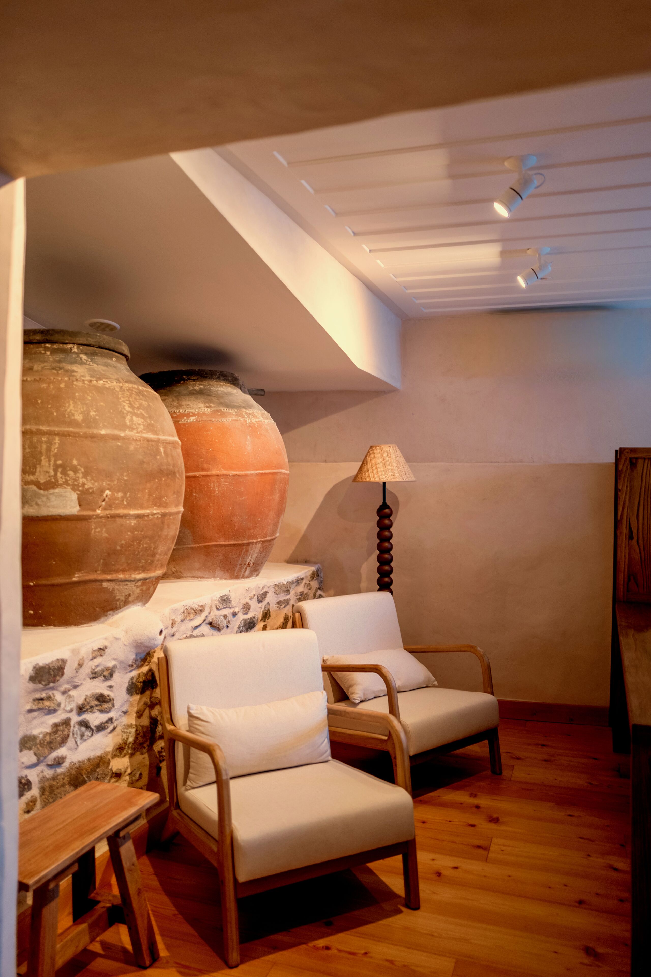 A room with a sloped ceiling, two wooden chairs, a table, and large clay pots against a wall.
