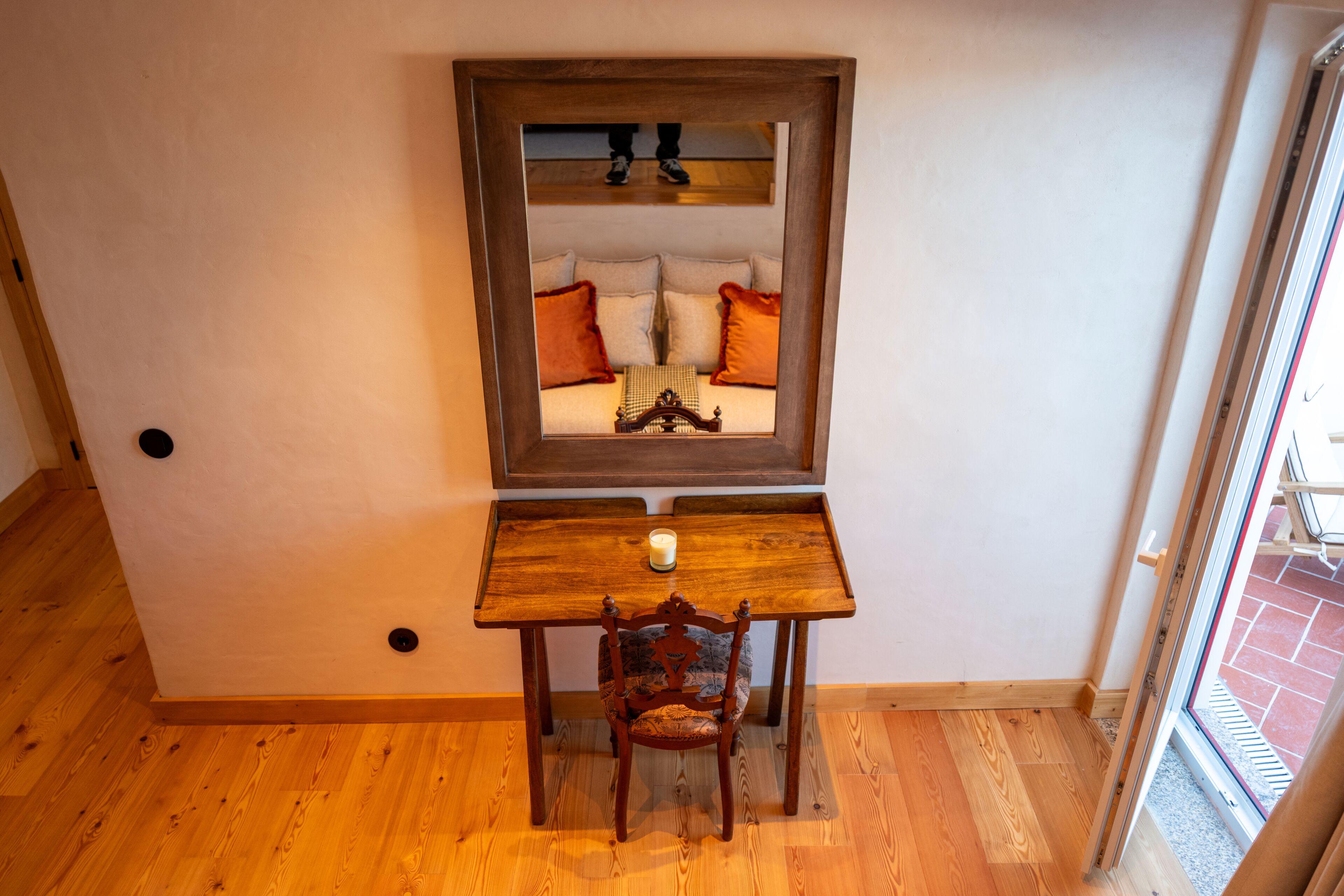 A room with a wooden desk, a chair, a mirror, and a window.