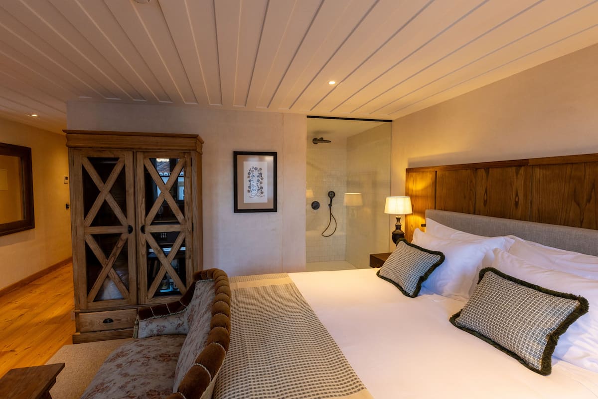 A hotel room with a bed, a wooden wardrobe, a shower, and a framed picture on the wall.