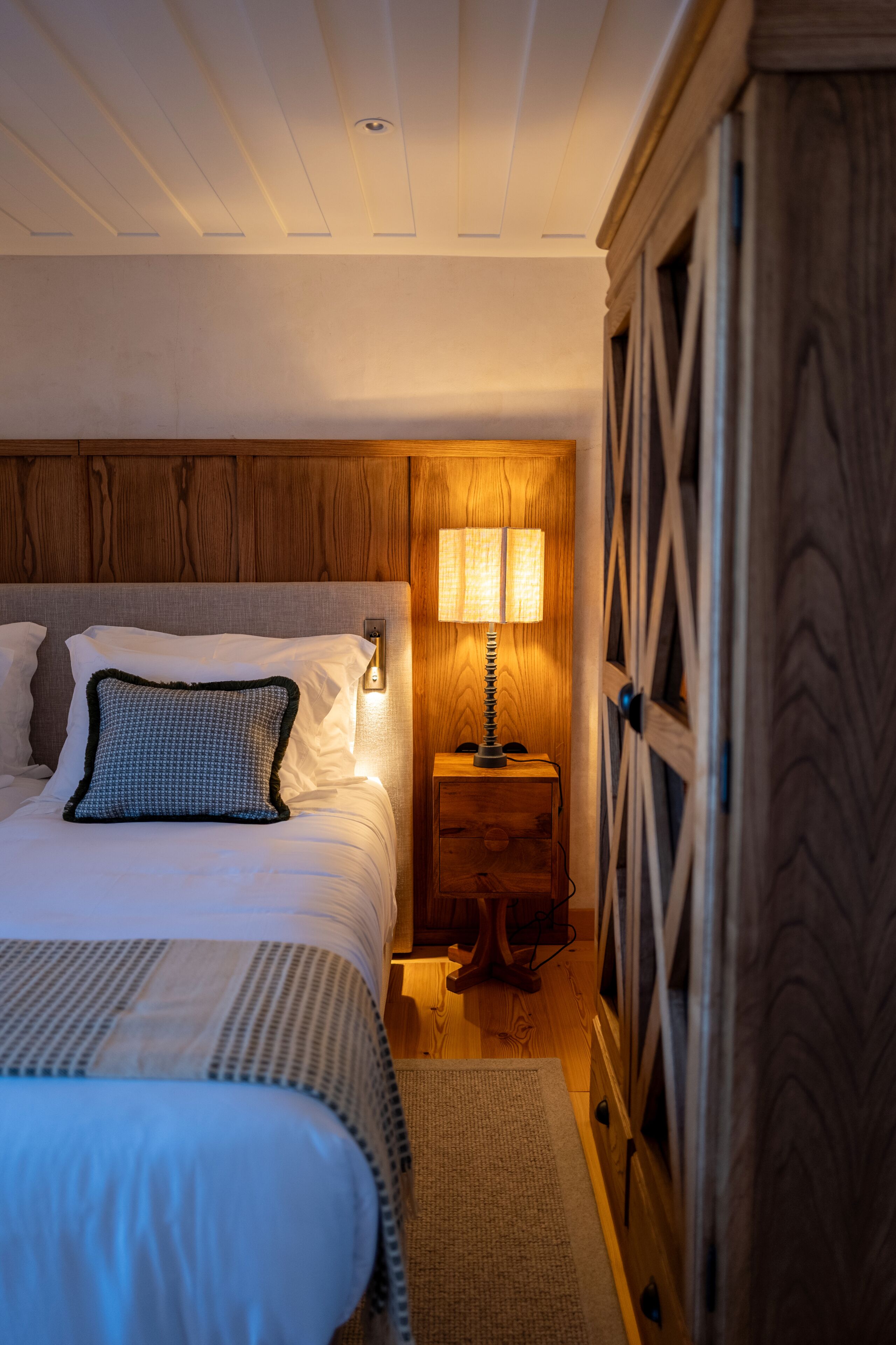 A bedroom with a bed, a nightstand with a lamp, and a wardrobe.