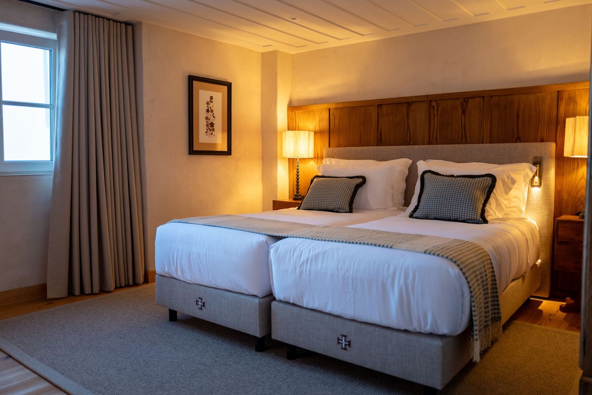 A double bed with a wooden headboard, two bedside tables with lamps, a framed picture on the wall, and a window with curtains.