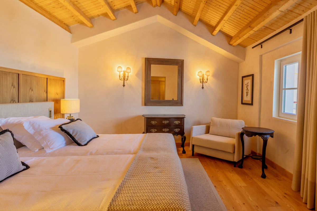 A bedroom with a large bed, a dresser, a chair, a small table, and a mirror on the wall.