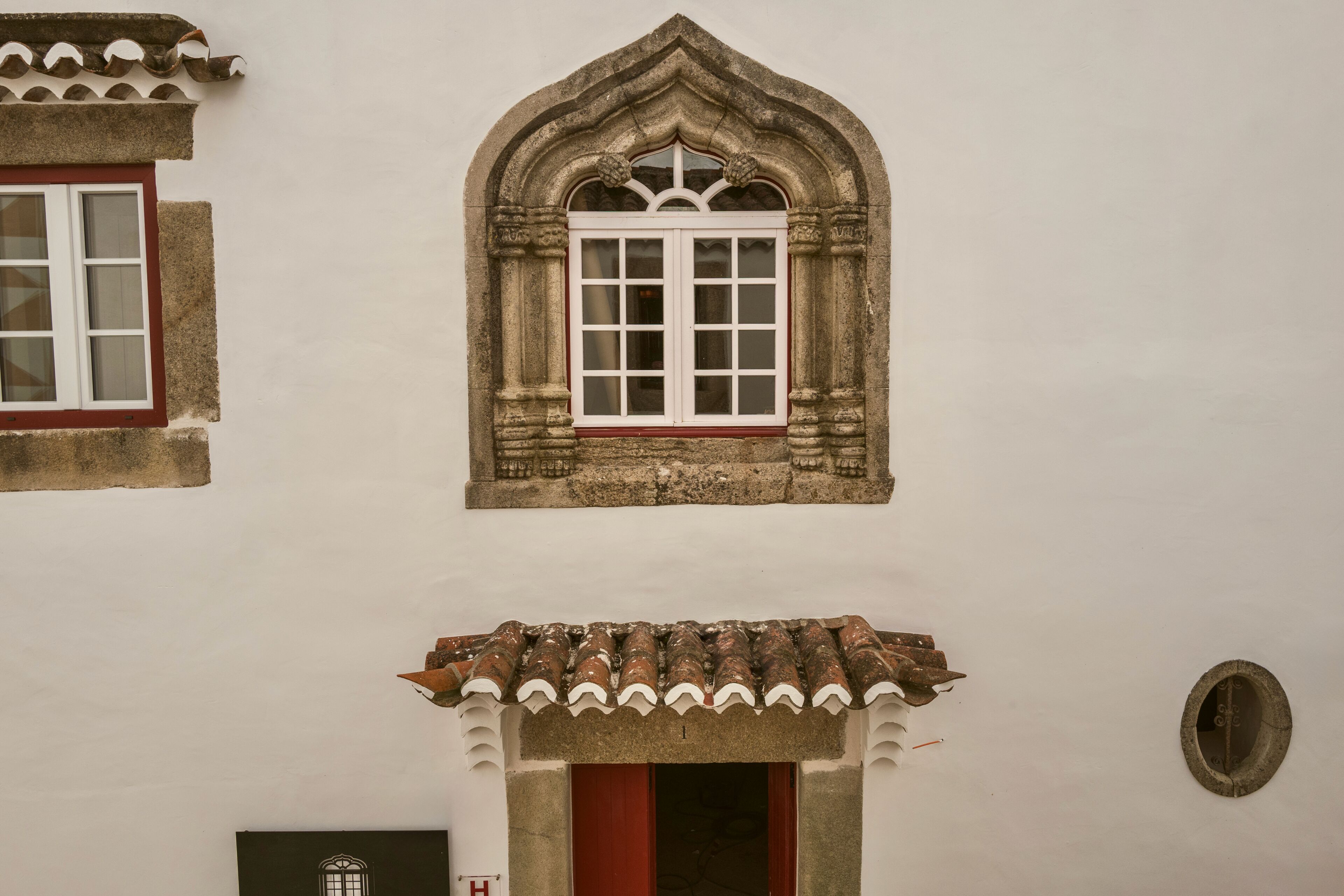 A building with a gothic window, a tiled roof, and a door with a red frame.