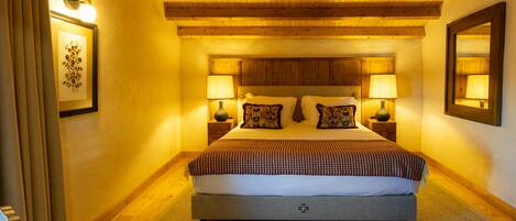 Un dormitorio con una cama grande, dos mesitas de noche con lámparas, vigas de madera en el techo y un cuadro enmarcado en la pared.