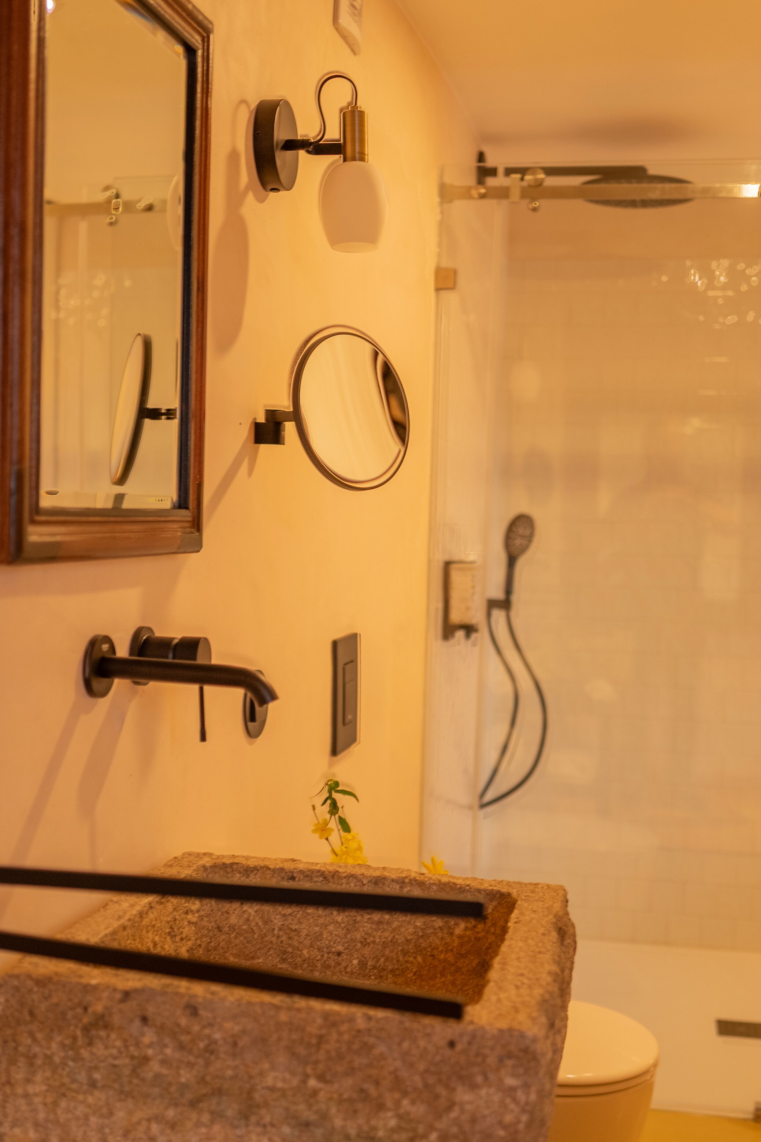 A bathroom with a stone sink, a mirror, a towel rack, a shower, and a toilet.