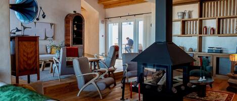 A cozy living room with a fireplace, wooden furniture, and a view through a glass door.