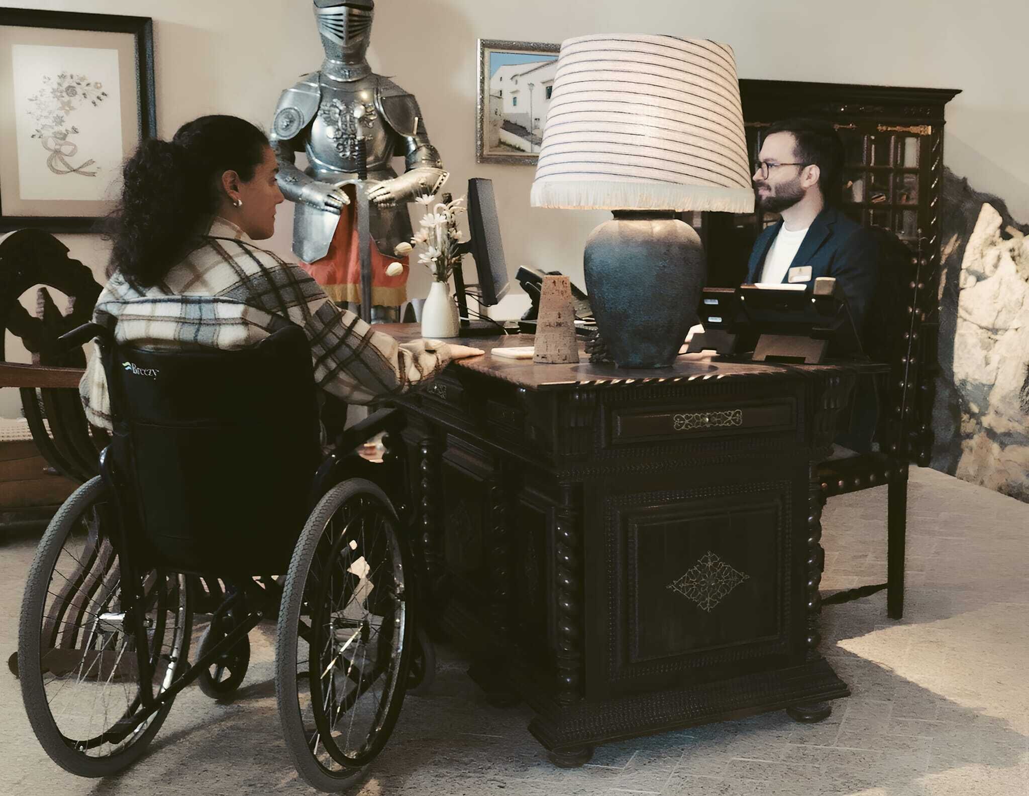 A room with a wheelchair, a desk with a lamp, and a knight statue.