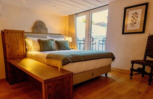 Un dormitorio con una cama de madera, una banca, cabecera, mesita de noche, lámpara, cuadro enmarcado y vista al exterior.