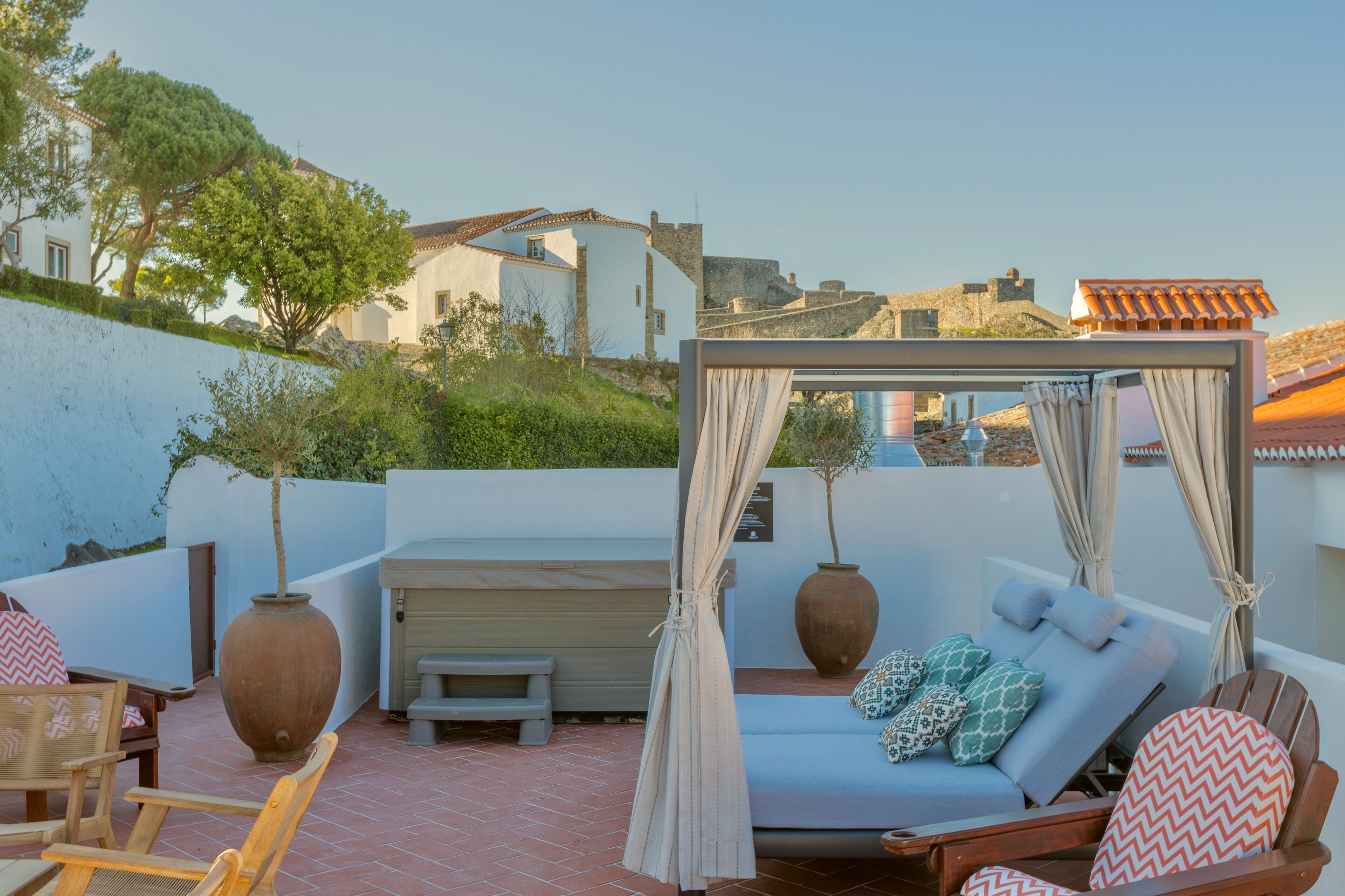 A rooftop terrace with a canopy bed, seating area, and large vases.