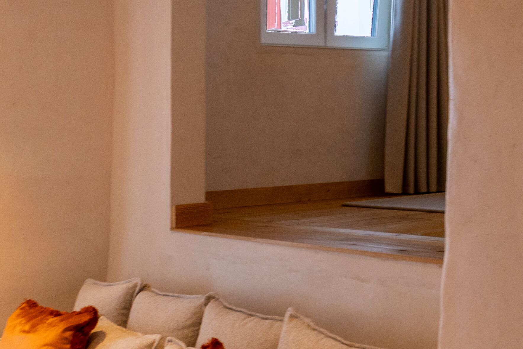 Una habitación con ventana, suelo de madera y un sofá con cojines.