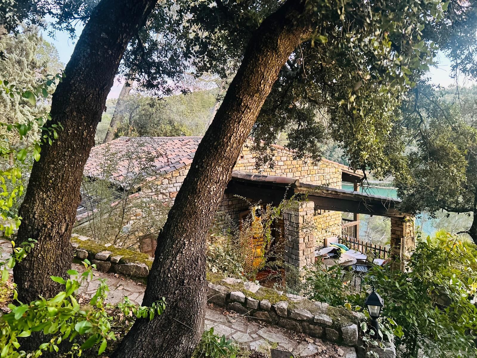Edifici de pedra rústic amb un porxo de fusta, envoltat d'arbres i una paret de pedra.
