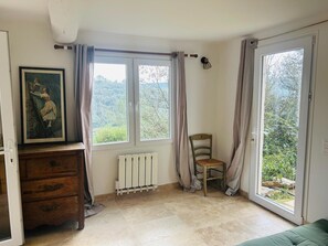 A room with a wooden dresser, a chair, a radiator, and a large window with curtains. - Charming house on Lake Carces (Carcès)