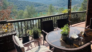 Ein Balkon mit Korbmöbeln, Blumentöpfen und einem Glastisch mit einem Weinglas.