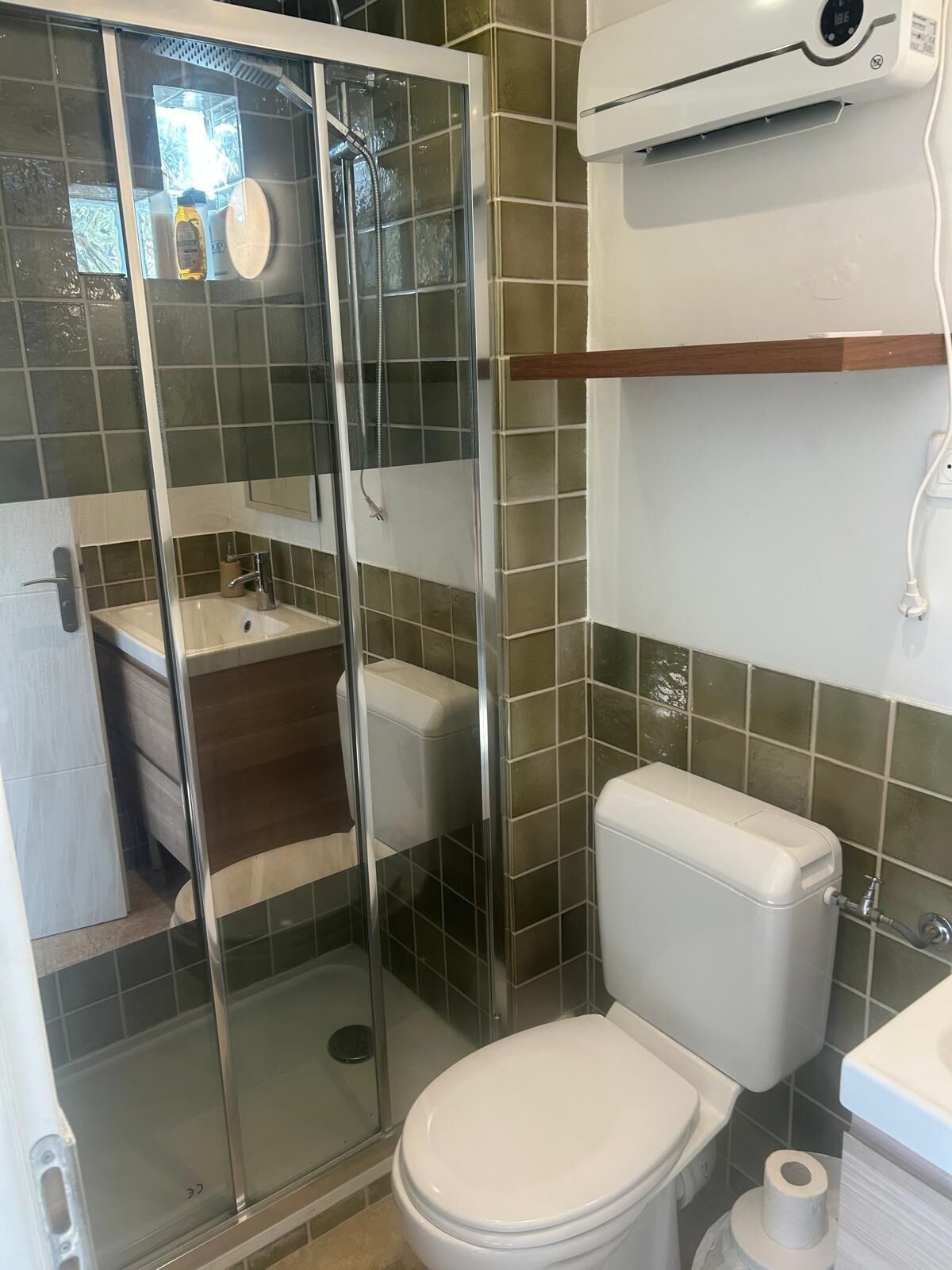 A bathroom with a glass-enclosed shower, a toilet, a sink, and a wall-mounted air conditioning unit.