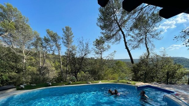 Ein Schwimmbecken mit klarem, blauem Wasser, umgeben von Bäumen und Blick auf die Landschaft.
