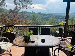 Ein runder Tisch mit Stühlen auf einem Balkon, umgeben von einem Holgitter, mit Blick auf eine bewaldete Landschaft.