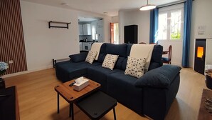 Een moderne woonkamer met een hoekbank, een kleine houten tafel, een open haard en een keuken op de achtergrond.
