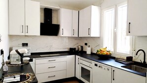 Een moderne keuken met witte kasten, een zwart aanrecht, een vaatwasser en een raam met natuurlijk licht.