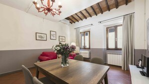 Ein Essbereich mit Holztisch, Stühlen, einer Blumenvase, einem roten Sofa und einer Chandelier.
