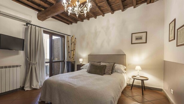 Ein Schlafzimmer mit Bett, Fernseher, einem Fenster mit Vorhängen, einer Chandelierleuchtre und einem Nachttisch mit Lampe.
