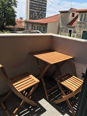 A balcony with a wooden table and two chairs, a stone wall, and a view of neighboring buildings. - Vibehaus Center of Split City Only 400m From Beach (Split)
