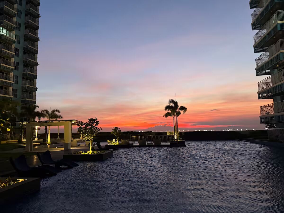 Un hotel frente al agua con vista al atardecer, asientos al aire libre y palmeras.