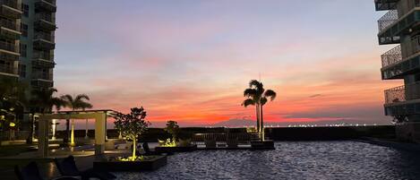 Un hotel frente al agua con vista al atardecer, asientos al aire libre y palmeras.