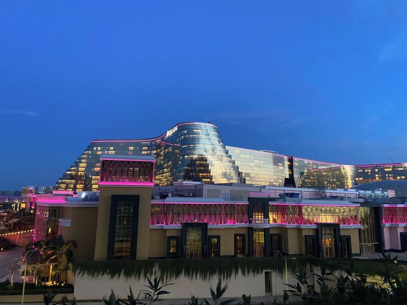 A modern hotel with a distinctive curved glass facade and pink lighting accents.