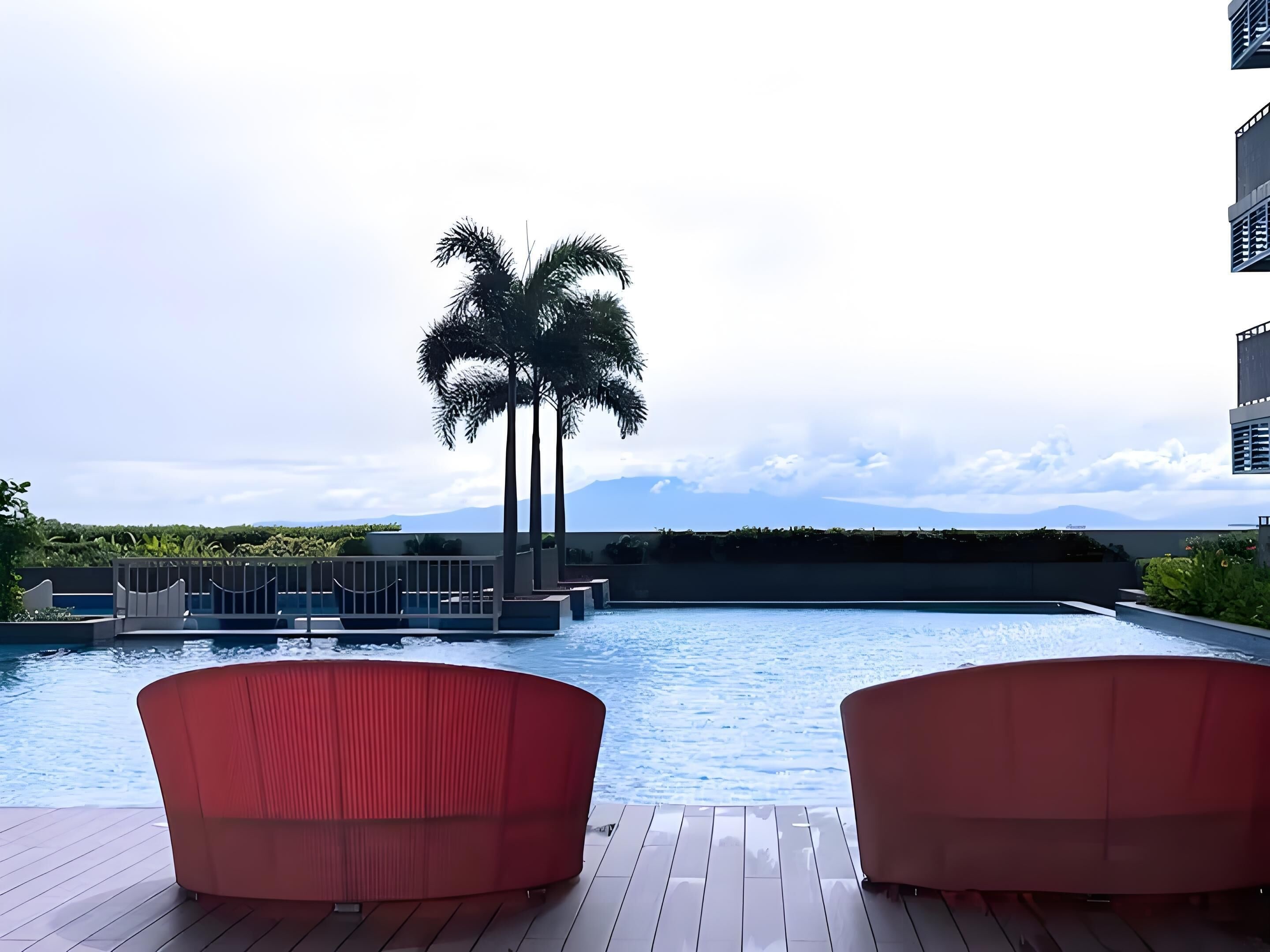 Una piscina con dos sillas rojas, una palmera y vistas a las montañas.