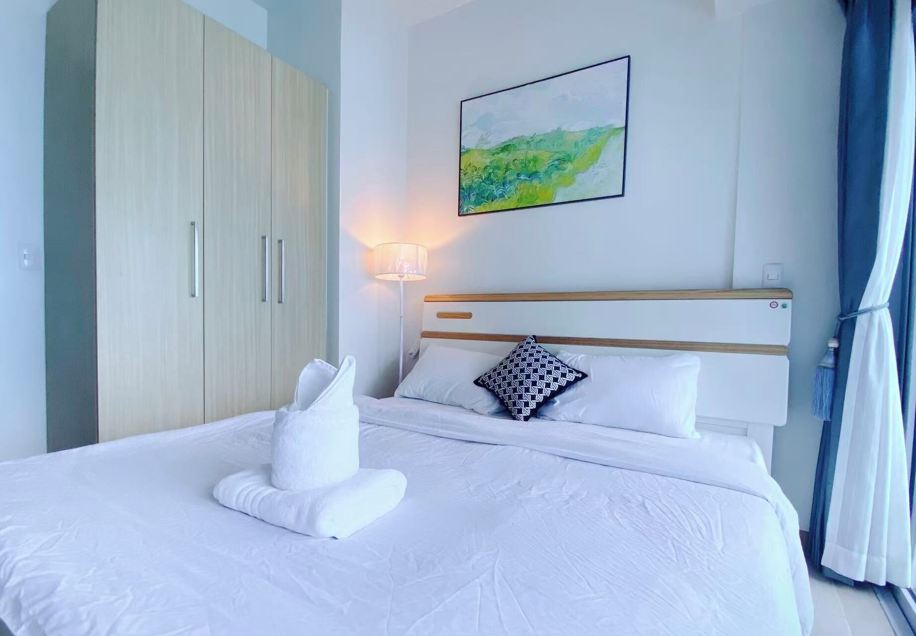 Una cama bien hecha con sábanas blancas, un cabecero de madera y un cuadro colgado en la pared.