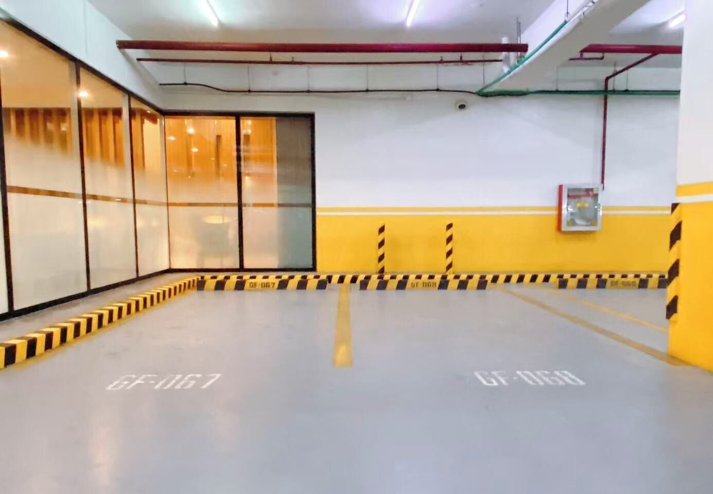 Un espacio interior amplio con una barrera rayada en amarillo y negro, divisiones de vidrio y un techo con tuberías a la vista.