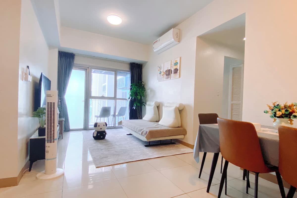 Una sala de estar moderna con sofá, mesa de comedor, sillas, una planta en maceta y una ventana con cortinas.