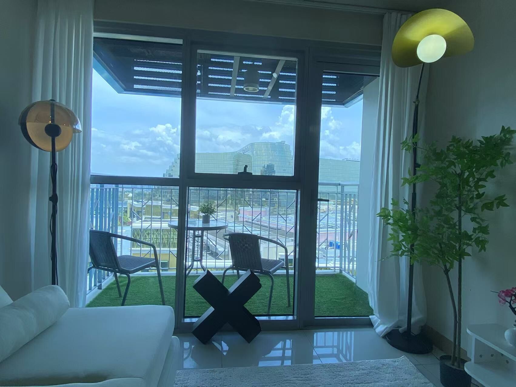 Une chambre moderne dotée d’une grande porte-fenêtre coulissante donnant sur un balcon, d’un canapé blanc, d’une petite table et d’une plante en pot.