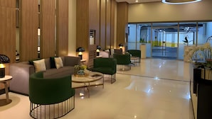 Egy modern előtér, amelyben kanapé, székek, egy kávézóasztal és egy recepciós pult található.